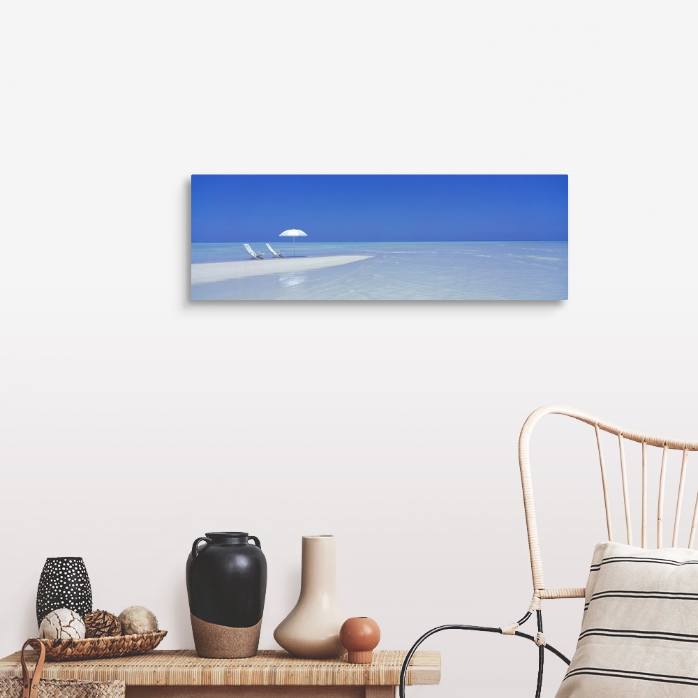 A farmhouse room featuring Large panoramic picture of two white chairs and a white beach umbrella sitting on sand that stret...