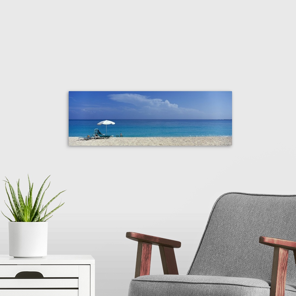 A modern room featuring Panoramic photograph of beach chairs and umbrella on sand with calm ocean in the distance.