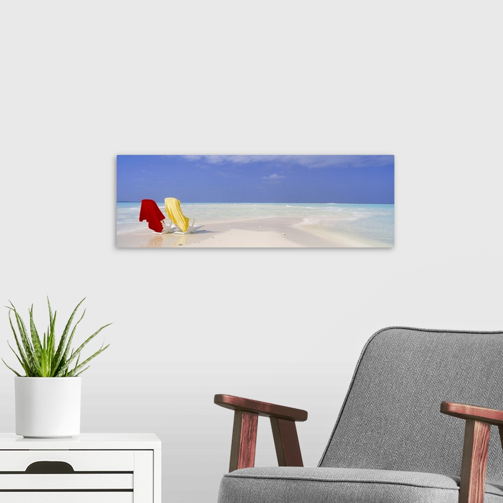 A modern room featuring An image of two beach chairs sitting on a sandbar with clear ocean water washing up on shore near...