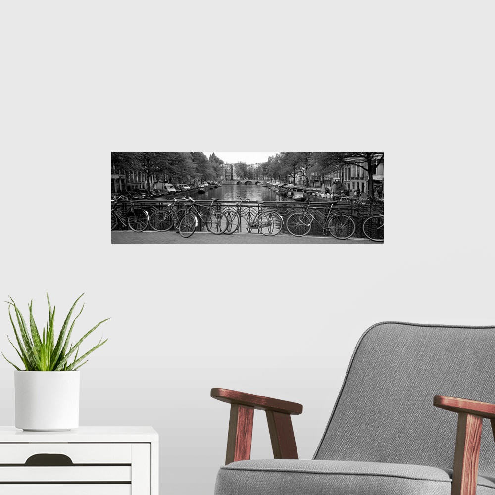 A modern room featuring Panoramic monochromatic photograph focuses on a group of bikes resting on an overpass over a rive...