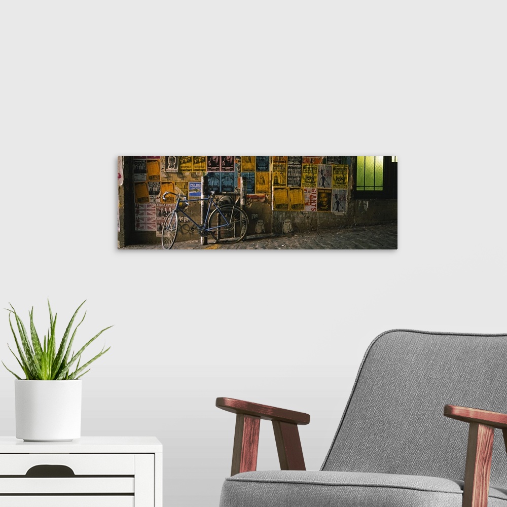 A modern room featuring This panoramic photograph is a cobblestoned street build on a slant and a wall covered in band po...