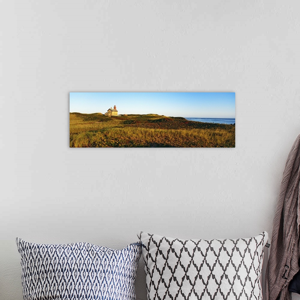 A bohemian room featuring A large lighthouse is photographed in panoramic view surrounded by open grassy land.