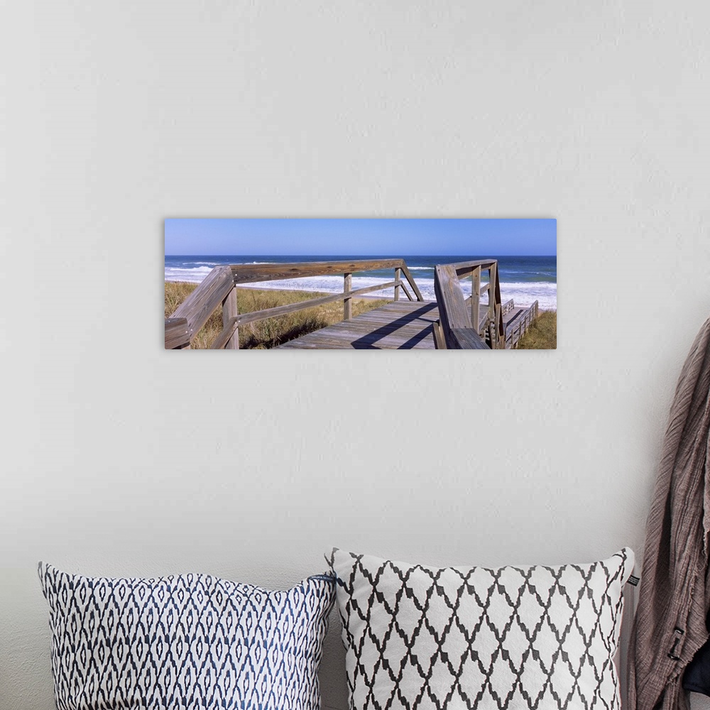 A bohemian room featuring Panoramic picture taken of a small walking bridge headed down toward the beach with dunes on eith...