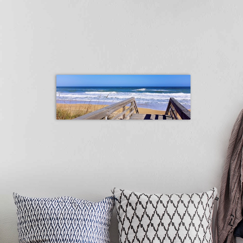 A bohemian room featuring Panoramic photo of a wooden walkway leading to a beach shore with crashing waves during the day.