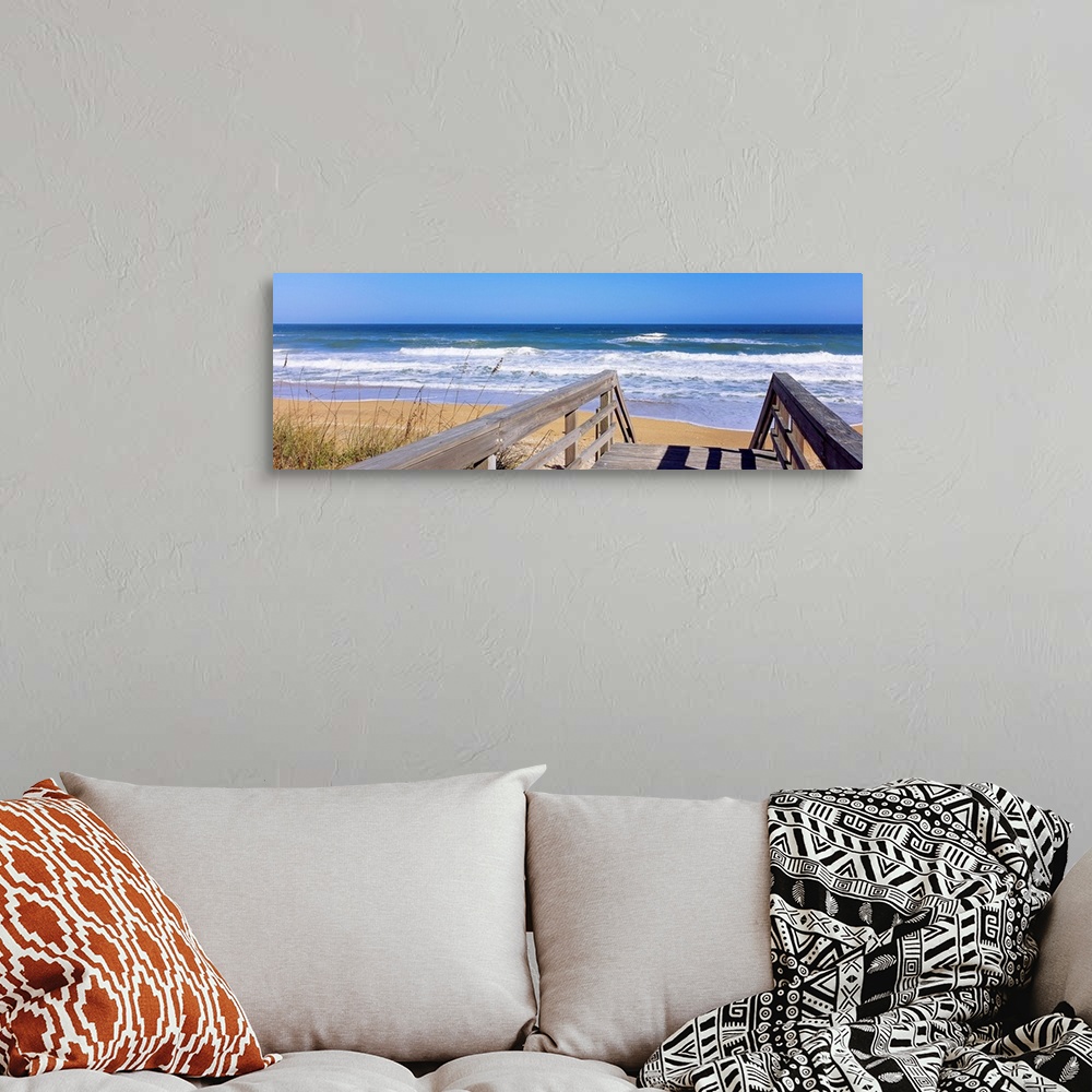 A bohemian room featuring Panoramic photo of a wooden walkway leading to a beach shore with crashing waves during the day.