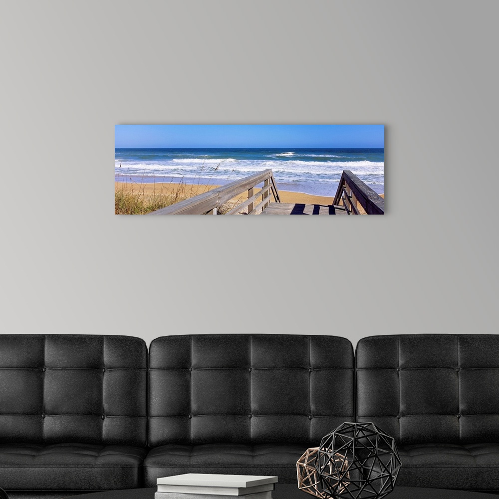 A modern room featuring Panoramic photo of a wooden walkway leading to a beach shore with crashing waves during the day.