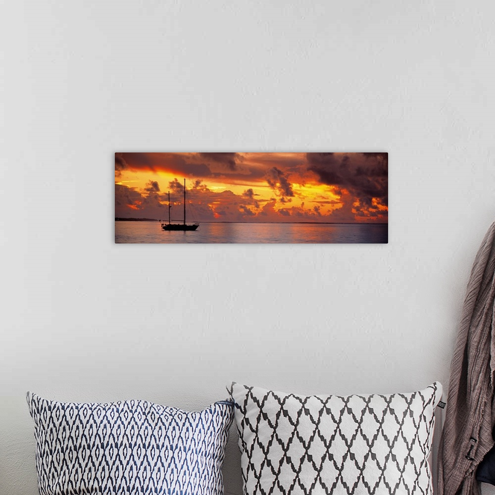 A bohemian room featuring Single ship with two tall masts on calm waters against a backdrop of dramatic fiery clouds at dusk.