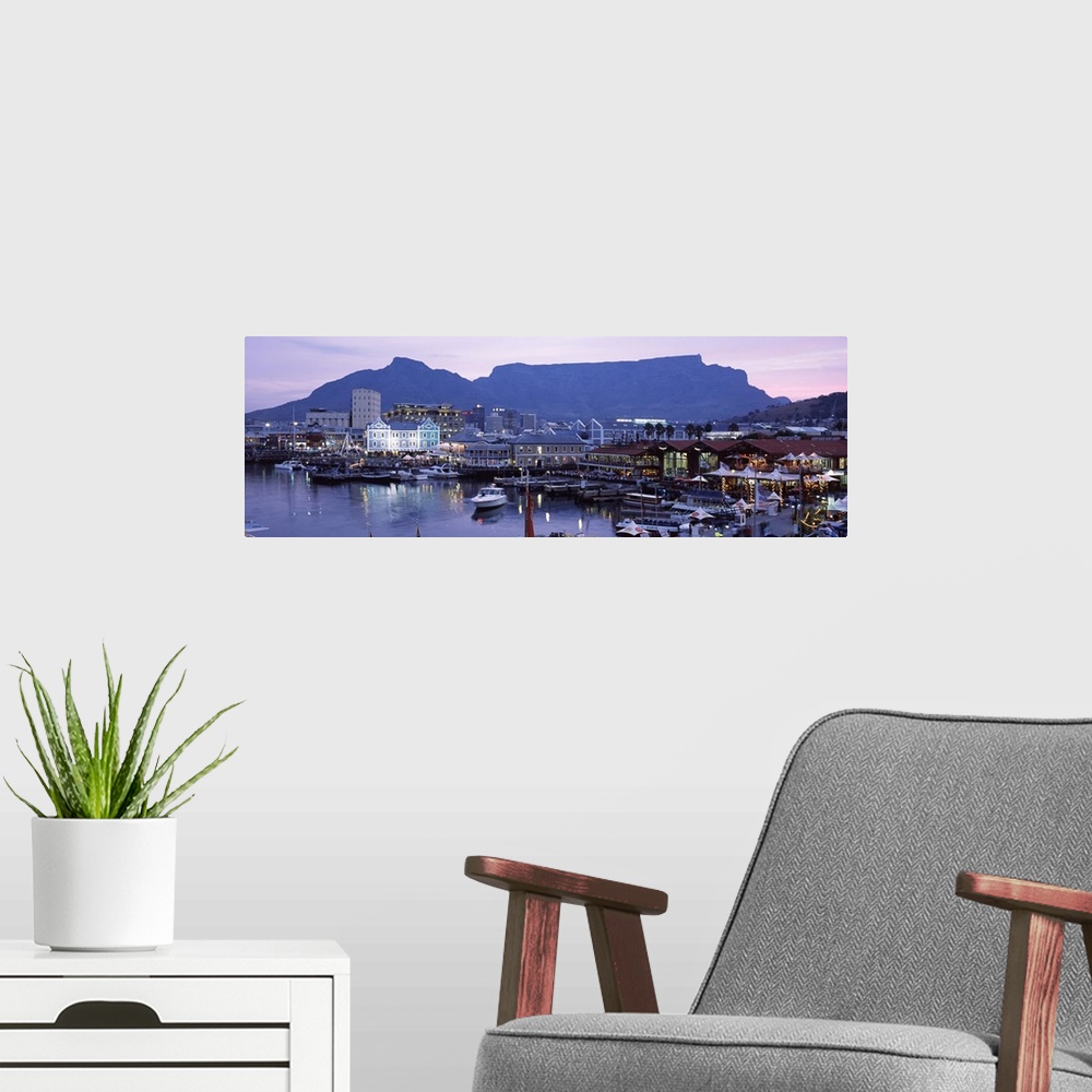 A modern room featuring Panoramic photograph of busy boat dock lit up at dusk with skyline and mountains in the distance.