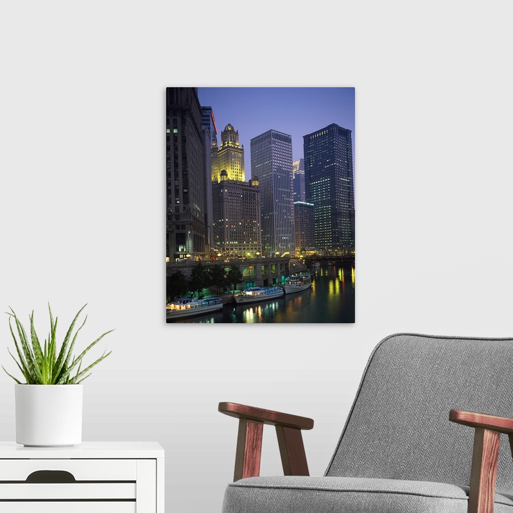A modern room featuring Portrait photograph on a big wall hanging of lit skyscrapers towering over the edge of the Chicag...