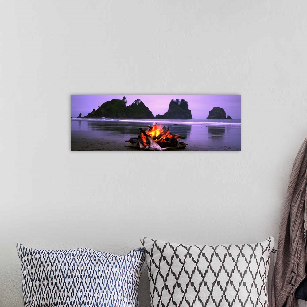 A bohemian room featuring Panoramic photograph displays a small blaze as it sits contained on a sandy beach in the Northwes...