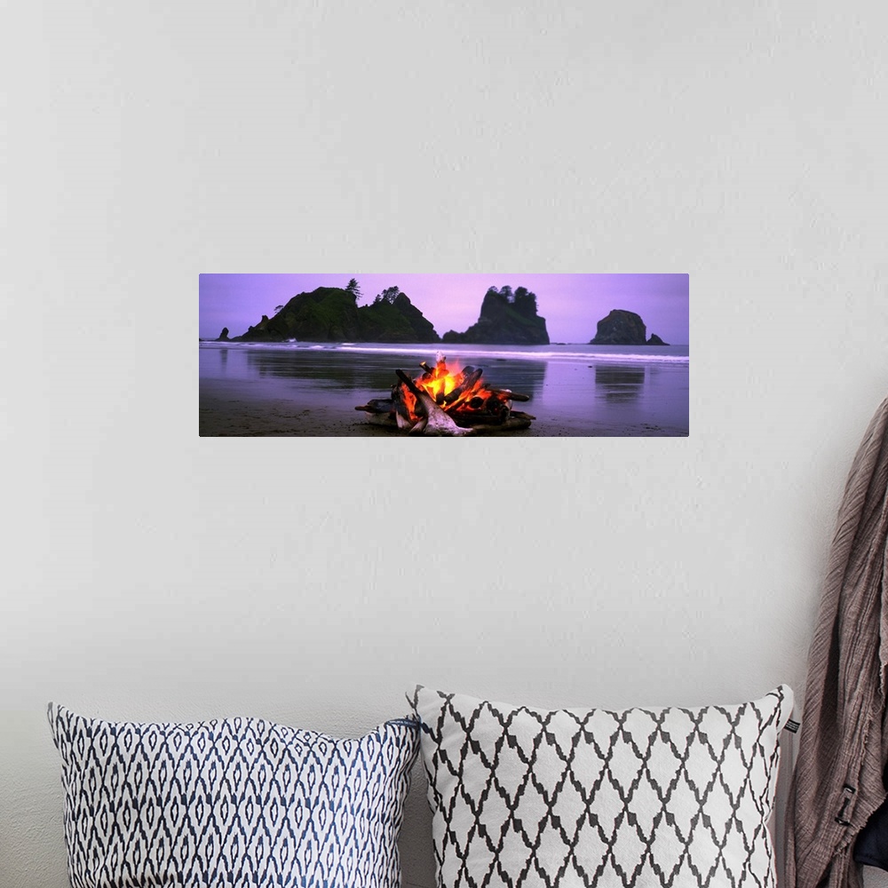 A bohemian room featuring Panoramic photograph displays a small blaze as it sits contained on a sandy beach in the Northwes...