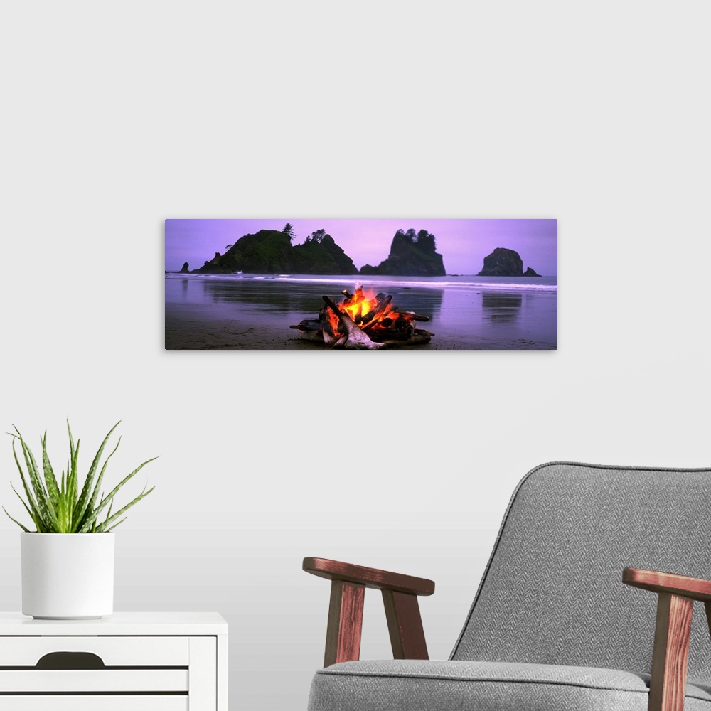 A modern room featuring Panoramic photograph displays a small blaze as it sits contained on a sandy beach in the Northwes...