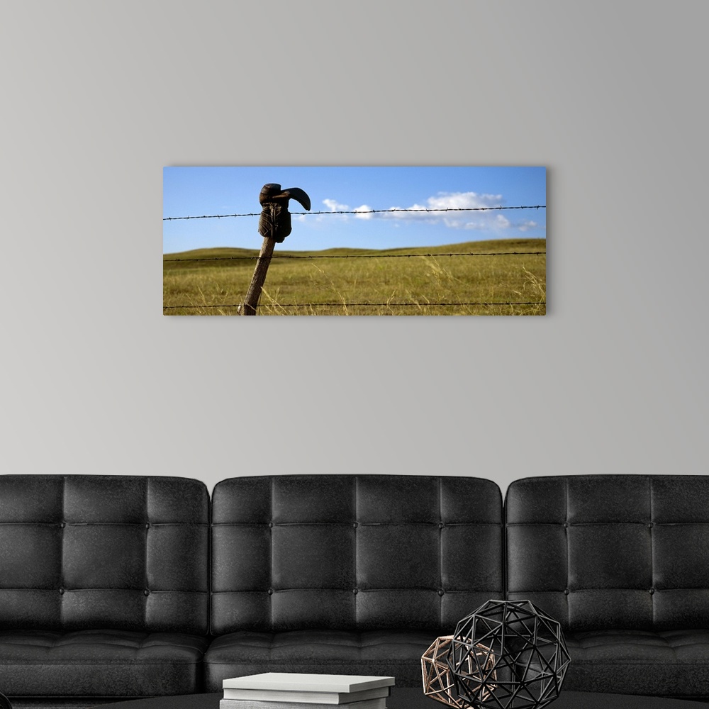 A modern room featuring Panoramic photograph of cowboy boot hanging upside down on a cable fence with grass covered hills...