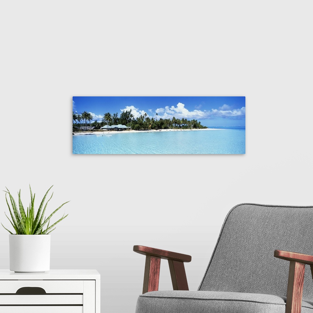 A modern room featuring A panoramic photograph of a tropical beach covered with palm trees and small open shelters surrou...