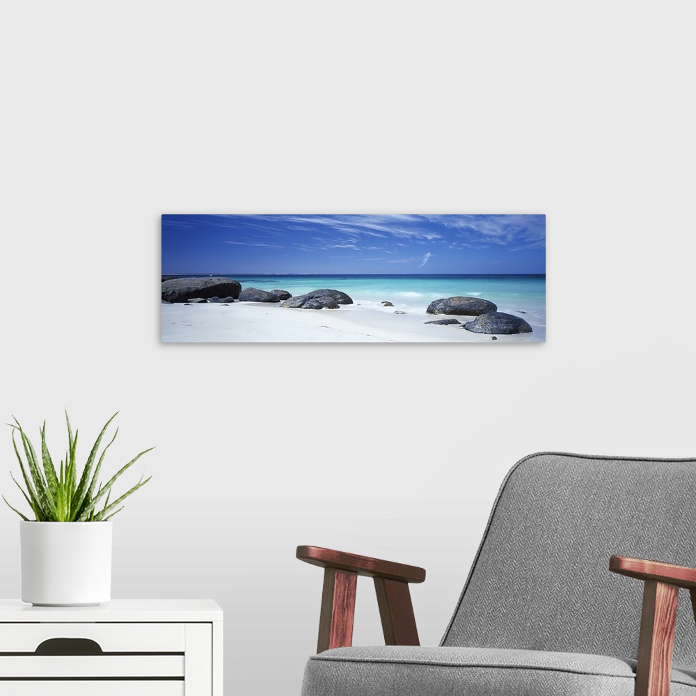 A modern room featuring Wide angle photograph on a large canvas of big rocks on a white sand beach near the crystal blue ...