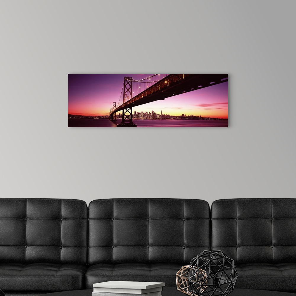 A modern room featuring Large panoramic photo print of a long bridge leading to a lit up city off in the distance at sunset.