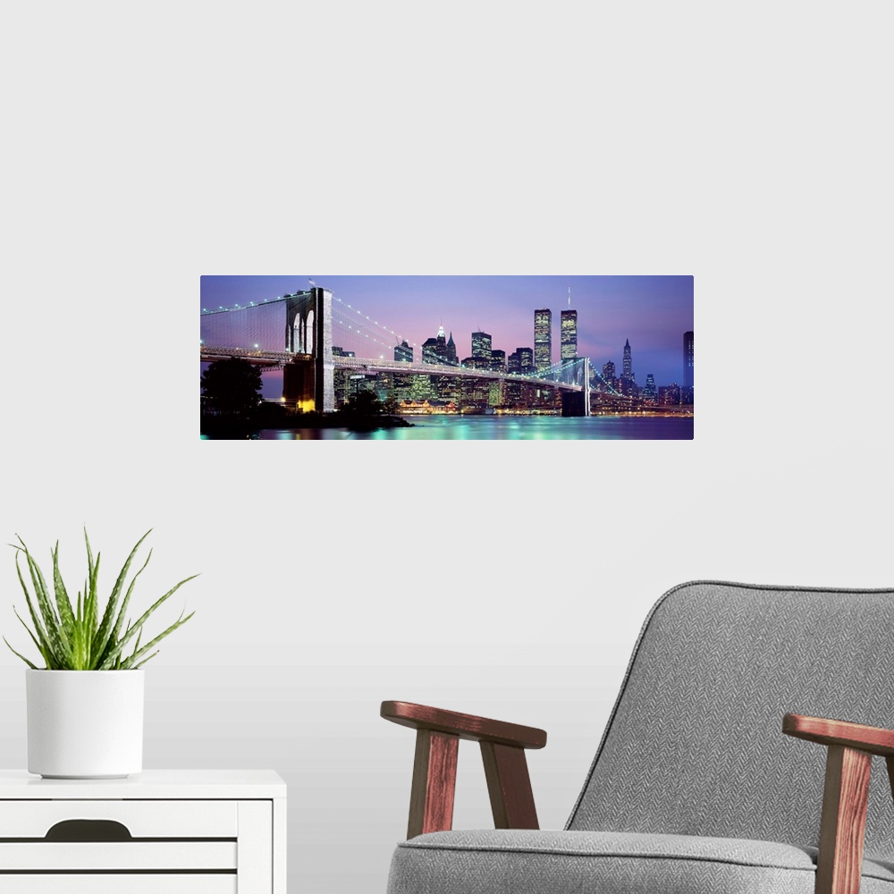 A modern room featuring Large panoramic view of the Brooklyn Bridge lit up at night.  The waters of the East River reflec...