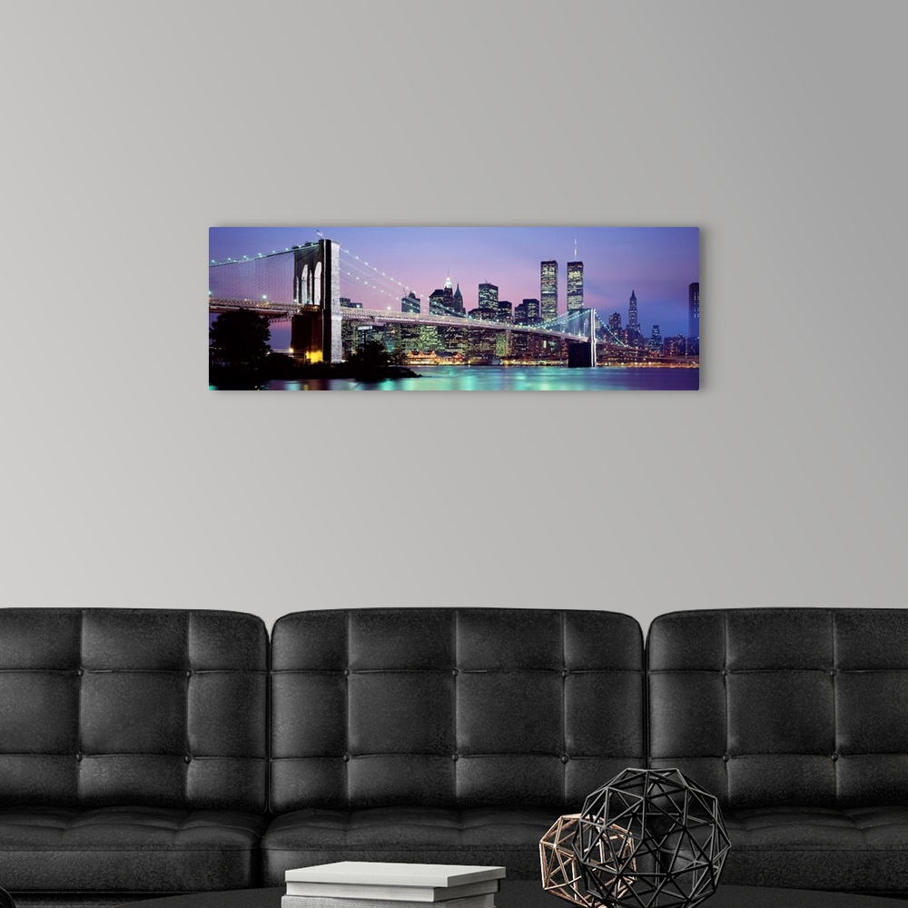 A modern room featuring Large panoramic view of the Brooklyn Bridge lit up at night.  The waters of the East River reflec...