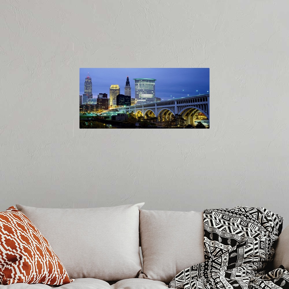 A bohemian room featuring A big canvas print of a long bridge entering a lit up city with building lights against a dusk sky.