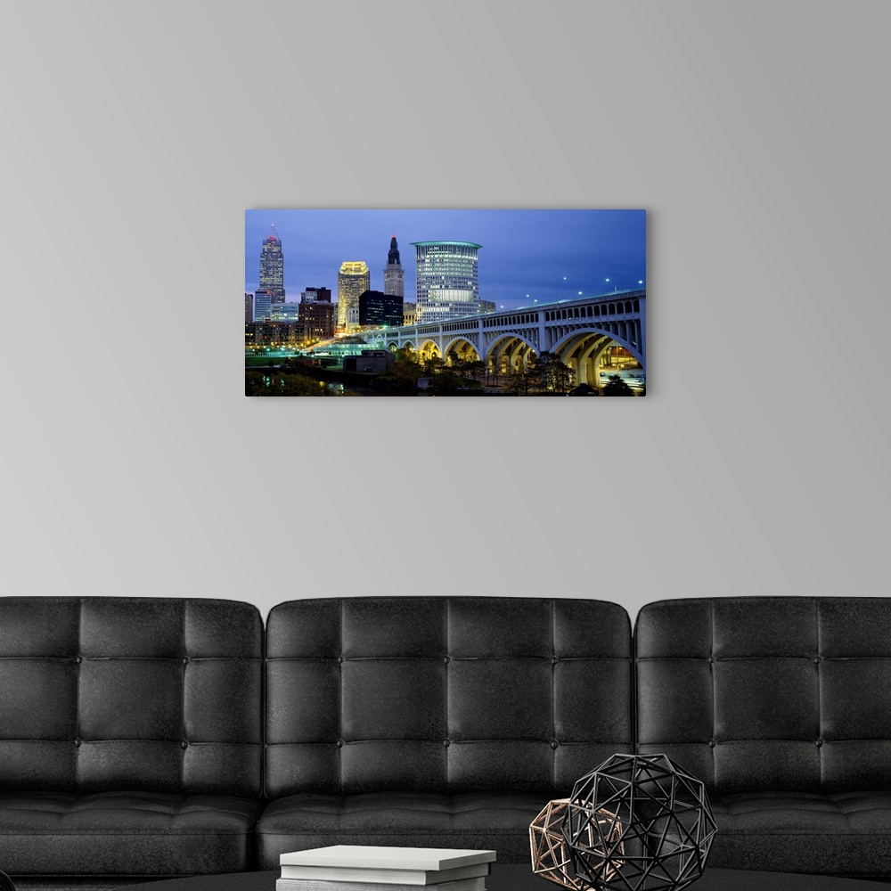 A modern room featuring A big canvas print of a long bridge entering a lit up city with building lights against a dusk sky.