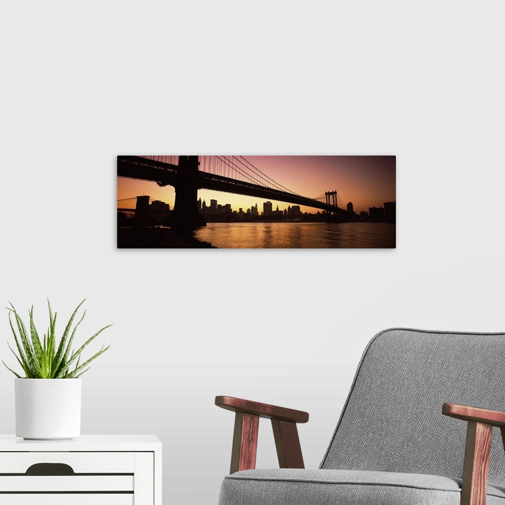 A modern room featuring The Manhattan bridge and New York City skyline are silhouetted by the sunset.