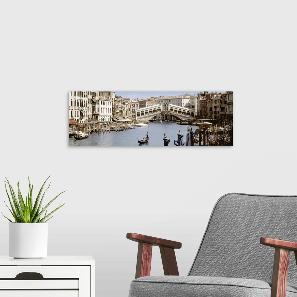 A modern room featuring Panoramic photograph taken of a walking bridge over a canal in Italy with gondola boat docks lini...
