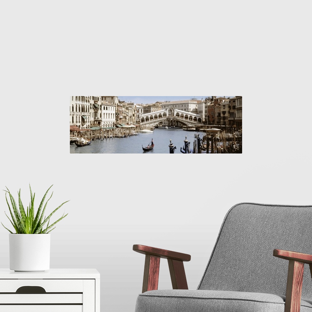 A modern room featuring Panoramic photograph taken of a walking bridge over a canal in Italy with gondola boat docks lini...