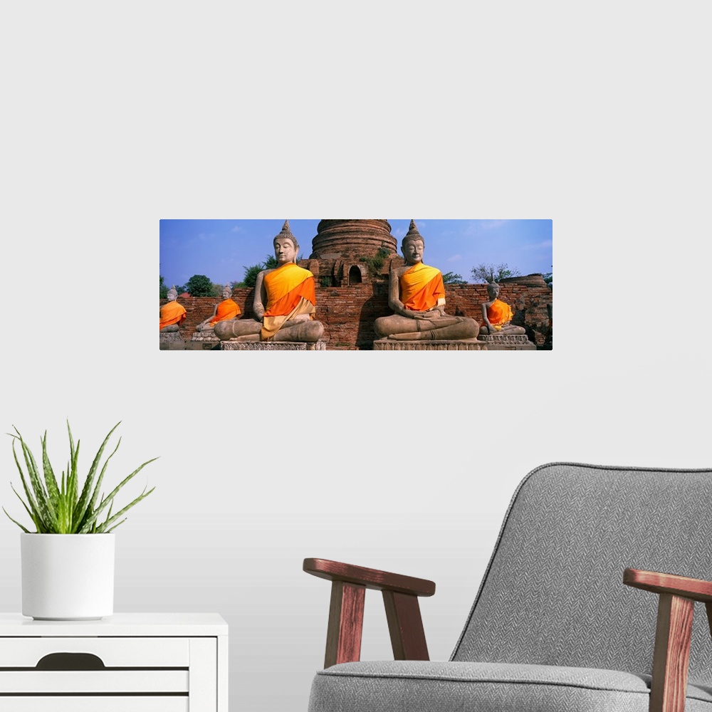 A modern room featuring Big horizontal photograph of many sitting Buddha statues, cloaked in golden orange fabric, a larg...