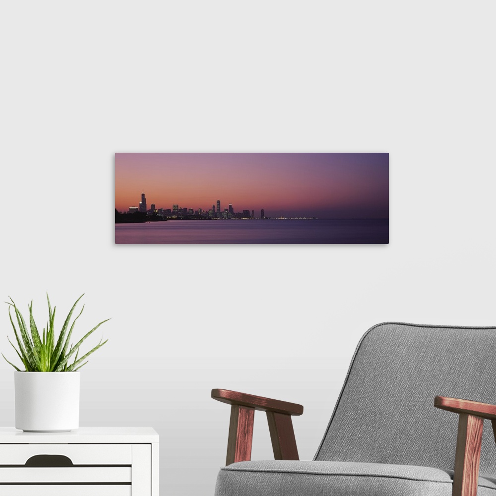 A modern room featuring The Chicago skyline is skewed to the left of this panoramic piece and silhouetted by a sunset sky...