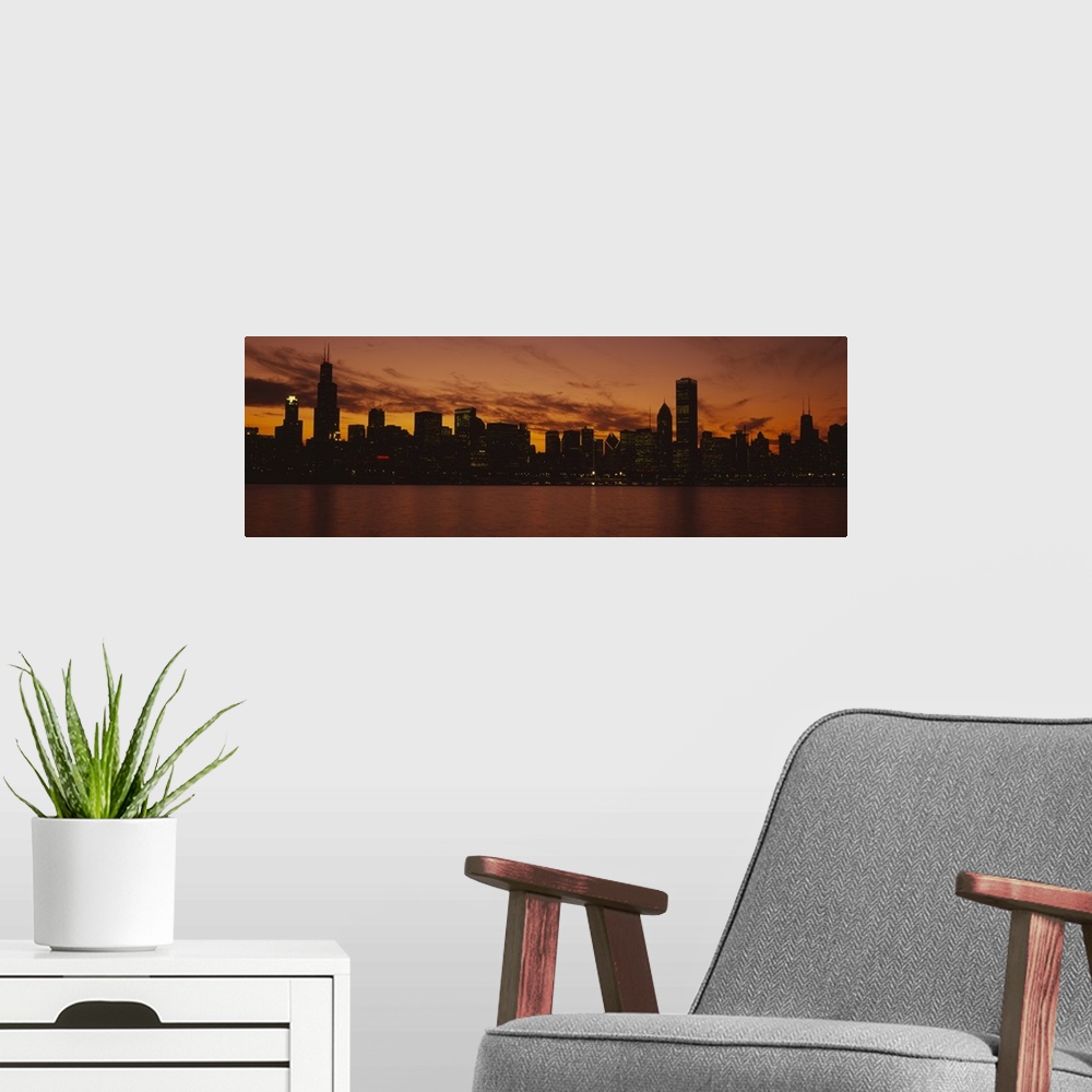 A modern room featuring Lake Michigan reflects the setting sun as lakeside buildings light up the night in downtown Chica...