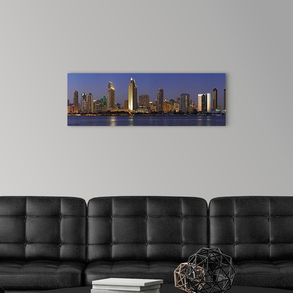 A modern room featuring Panoramic photograph of skyline at night with buildings lit up and reflected in the waterfront be...