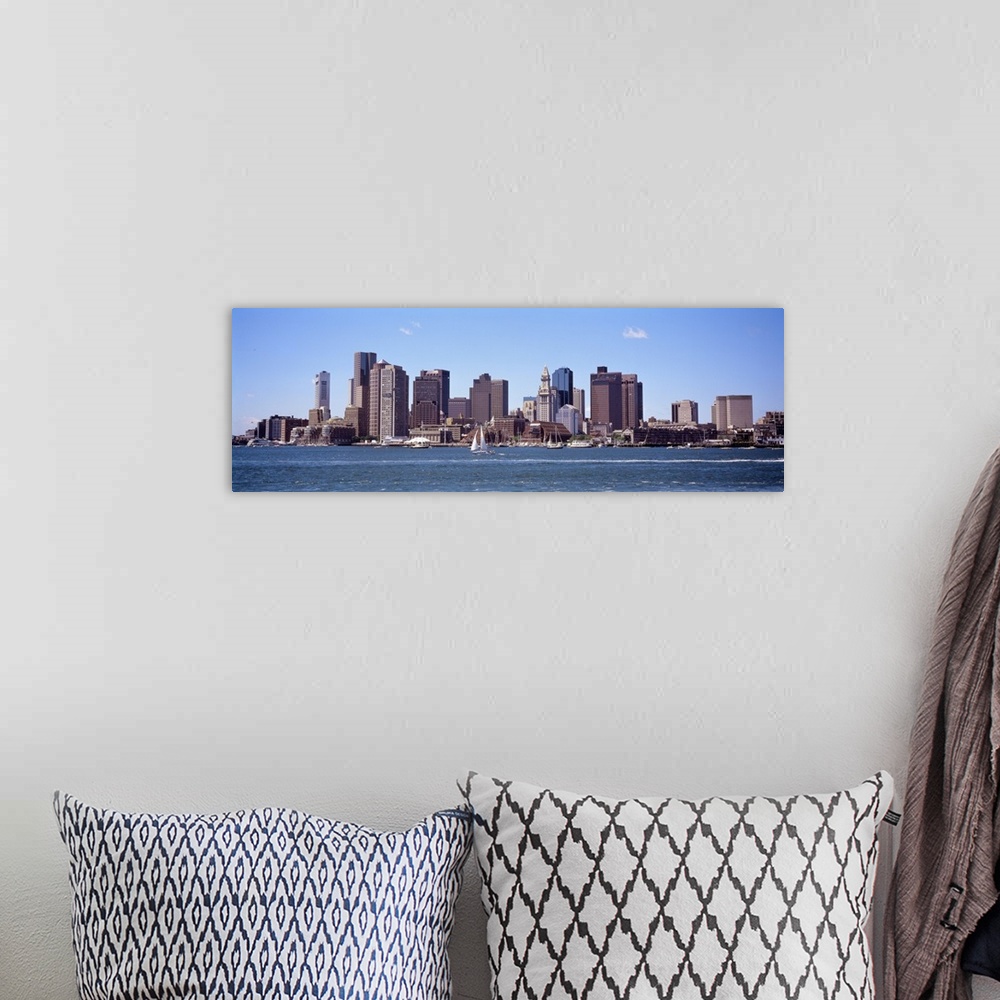A bohemian room featuring The Boston skyline is photographed from across the water on a beautiful sunny day with sail boats...