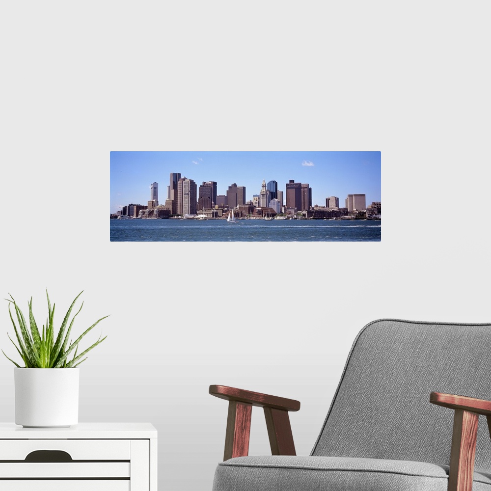 A modern room featuring The Boston skyline is photographed from across the water on a beautiful sunny day with sail boats...