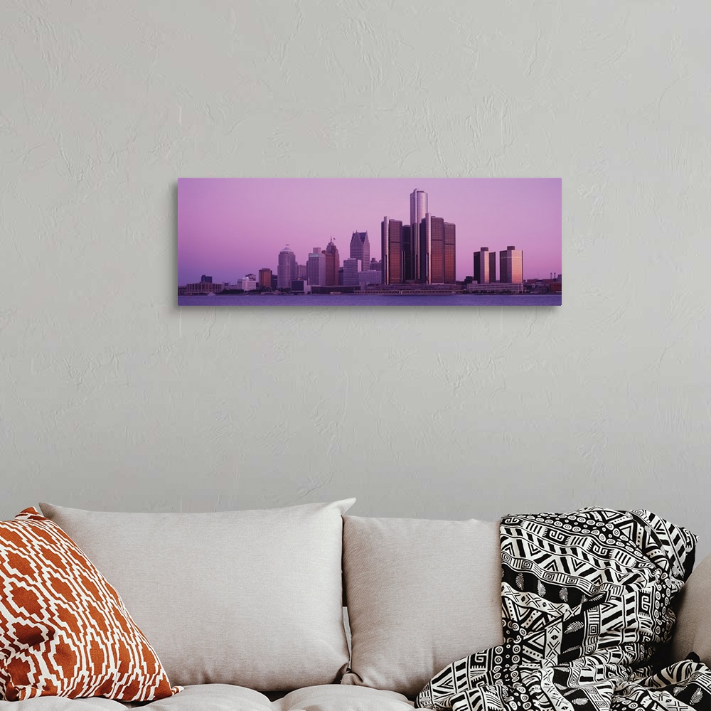 A bohemian room featuring The Detroit skyline is photographed in panoramic view from across the waterfront during dusk.