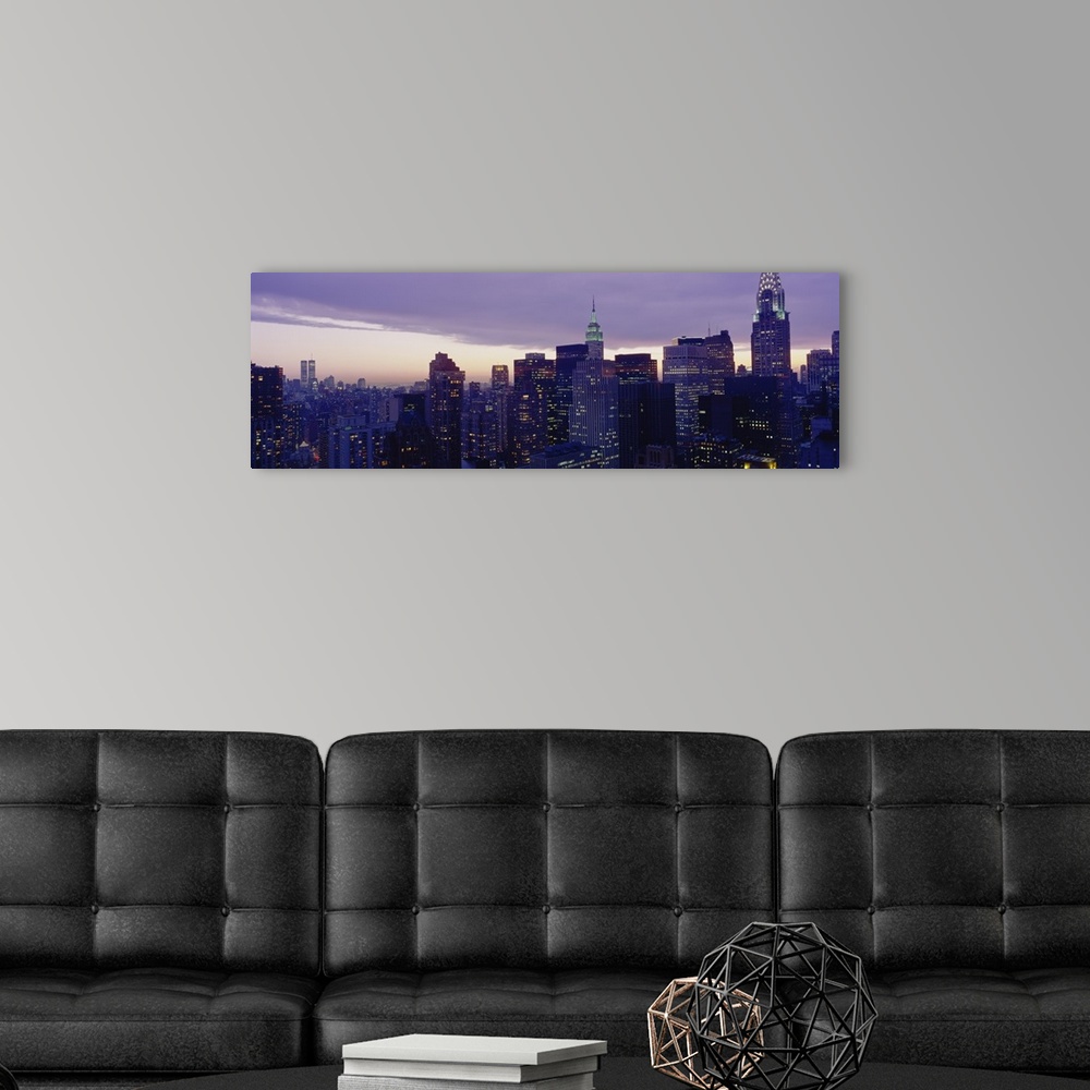 A modern room featuring A wide angle shot taken of the Manhattan skyline with the buildings lit up at night with a view o...