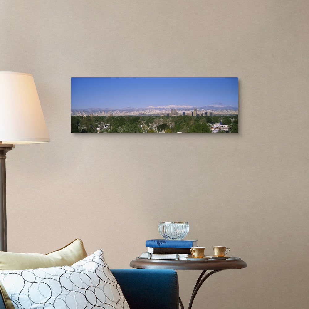 A traditional room featuring The city of Denver is photographed from a distance over trees and homes. Mountains are pictured f...