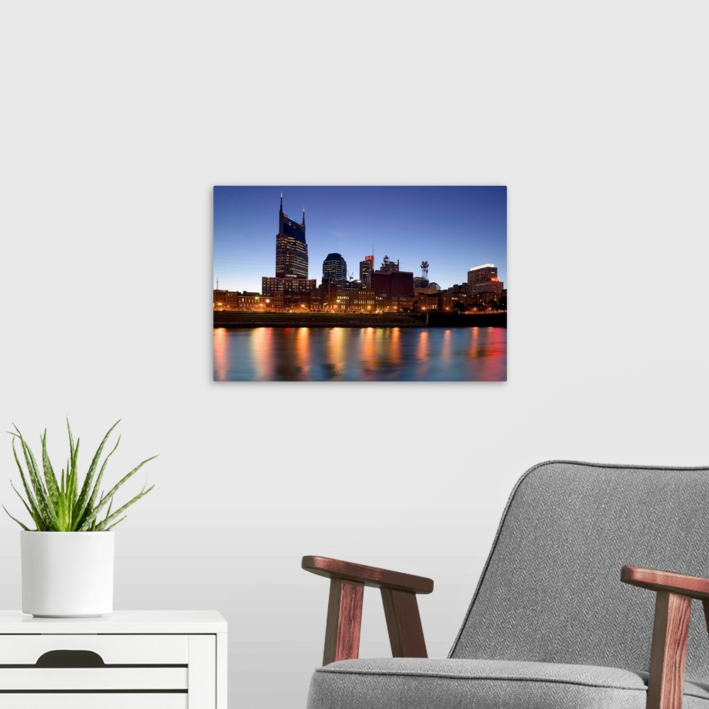 A modern room featuring This photograph city skyline lit up in the early twilight and the city lights reflect in the water.
