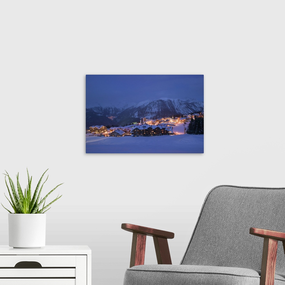 A modern room featuring Photograph of small town nestled at the bottom of snow covered mountain at night.
