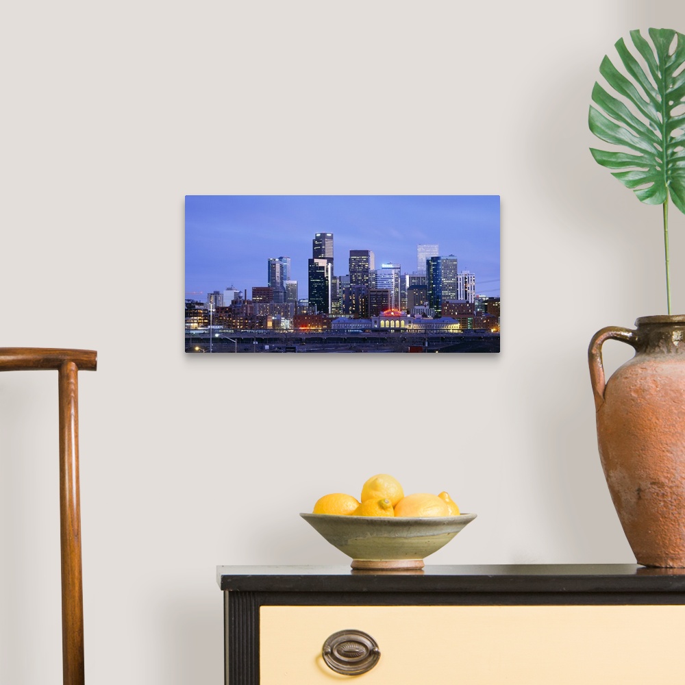 A traditional room featuring A large panoramic piece of a photograph of the Denver skyline with the buildings lit up during su...