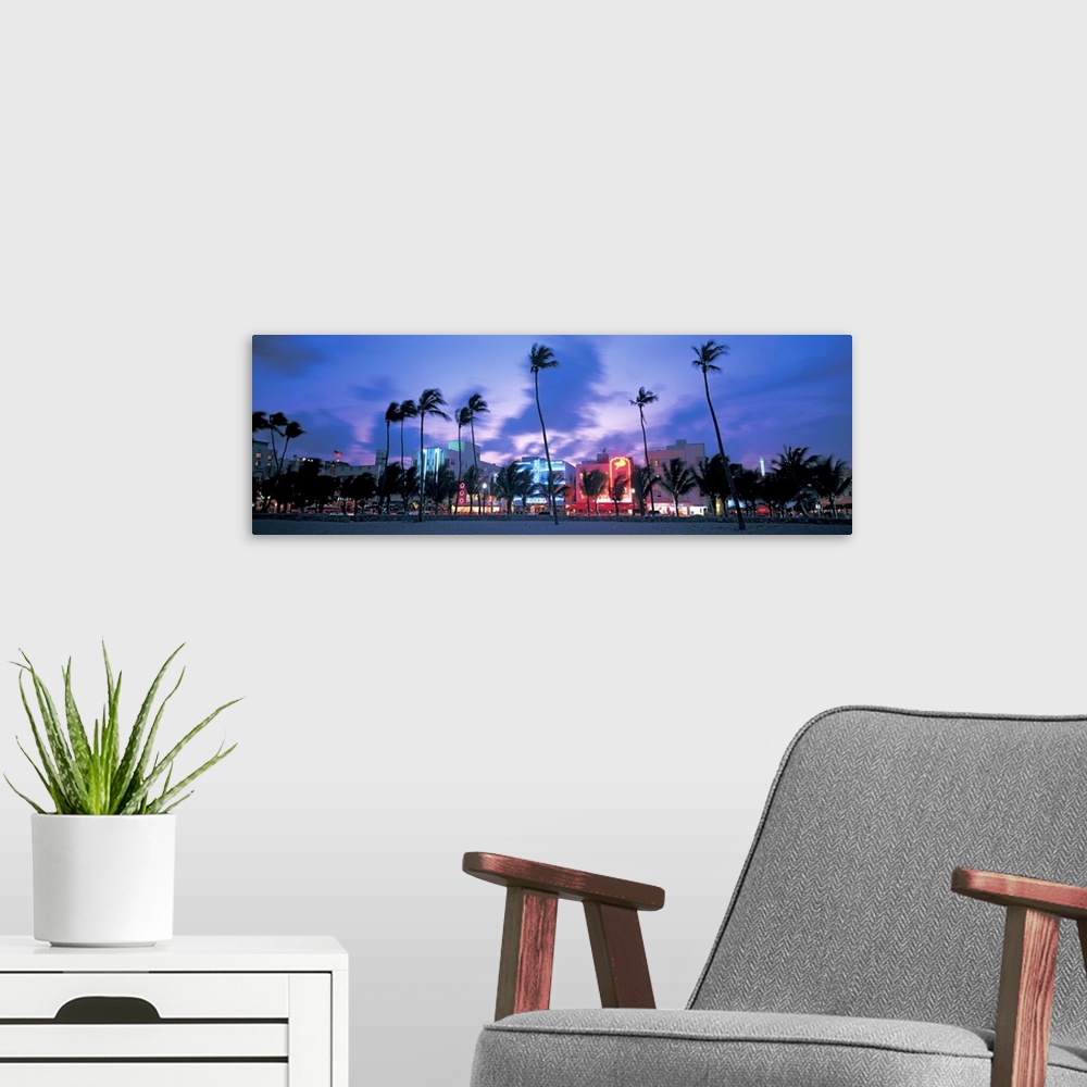 A modern room featuring Ocean Drive illuminated by neon lights at night and palm trees blowing in the wind off the ocean ...