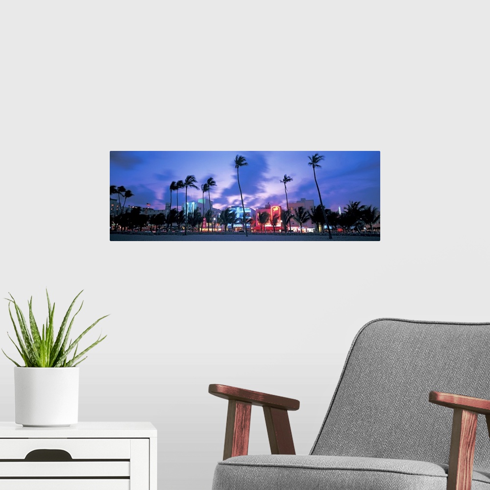 A modern room featuring Ocean Drive illuminated by neon lights at night and palm trees blowing in the wind off the ocean ...