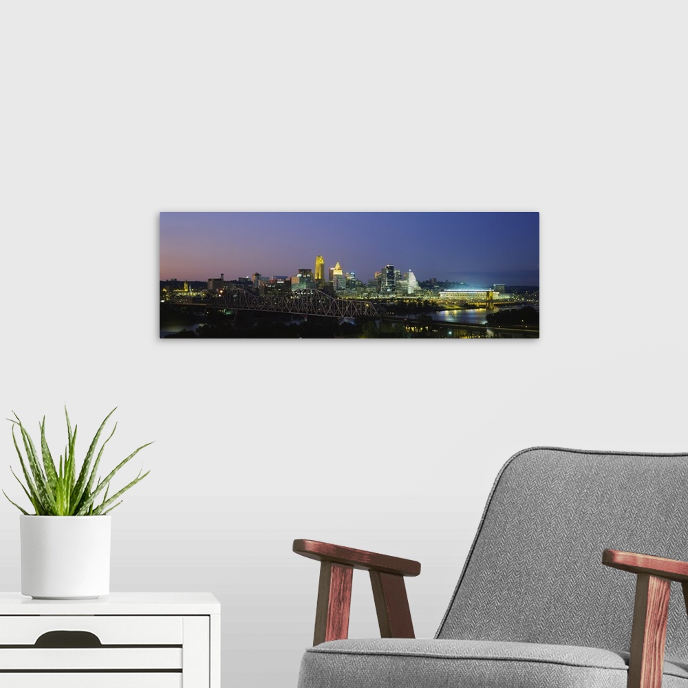 A modern room featuring The Cincinnati skyline is photographed in panoramic view and illuminated under a night sky.
