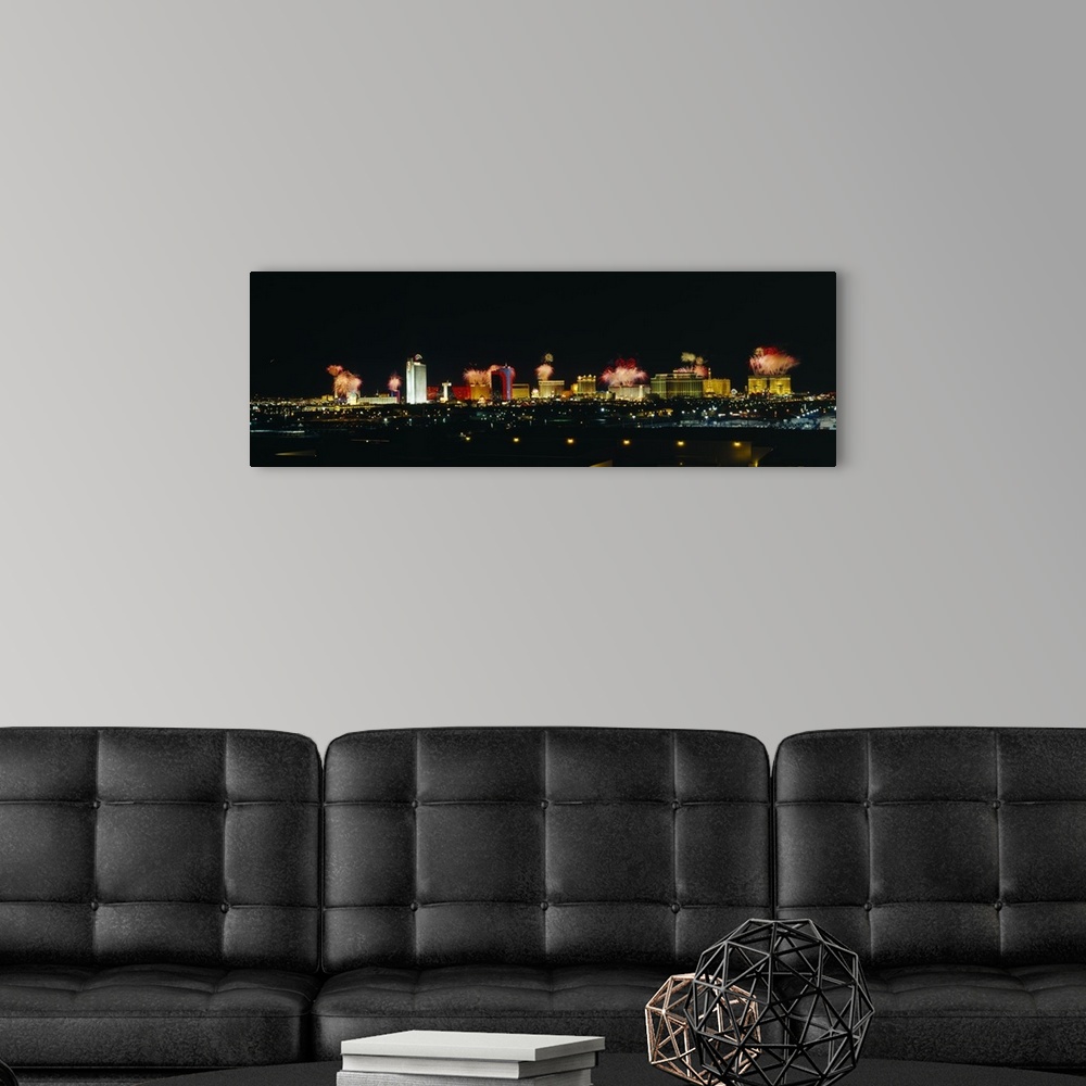 A modern room featuring A wide angle photograph taken of the Las Vegas strip at night with the buildings lit up and firew...