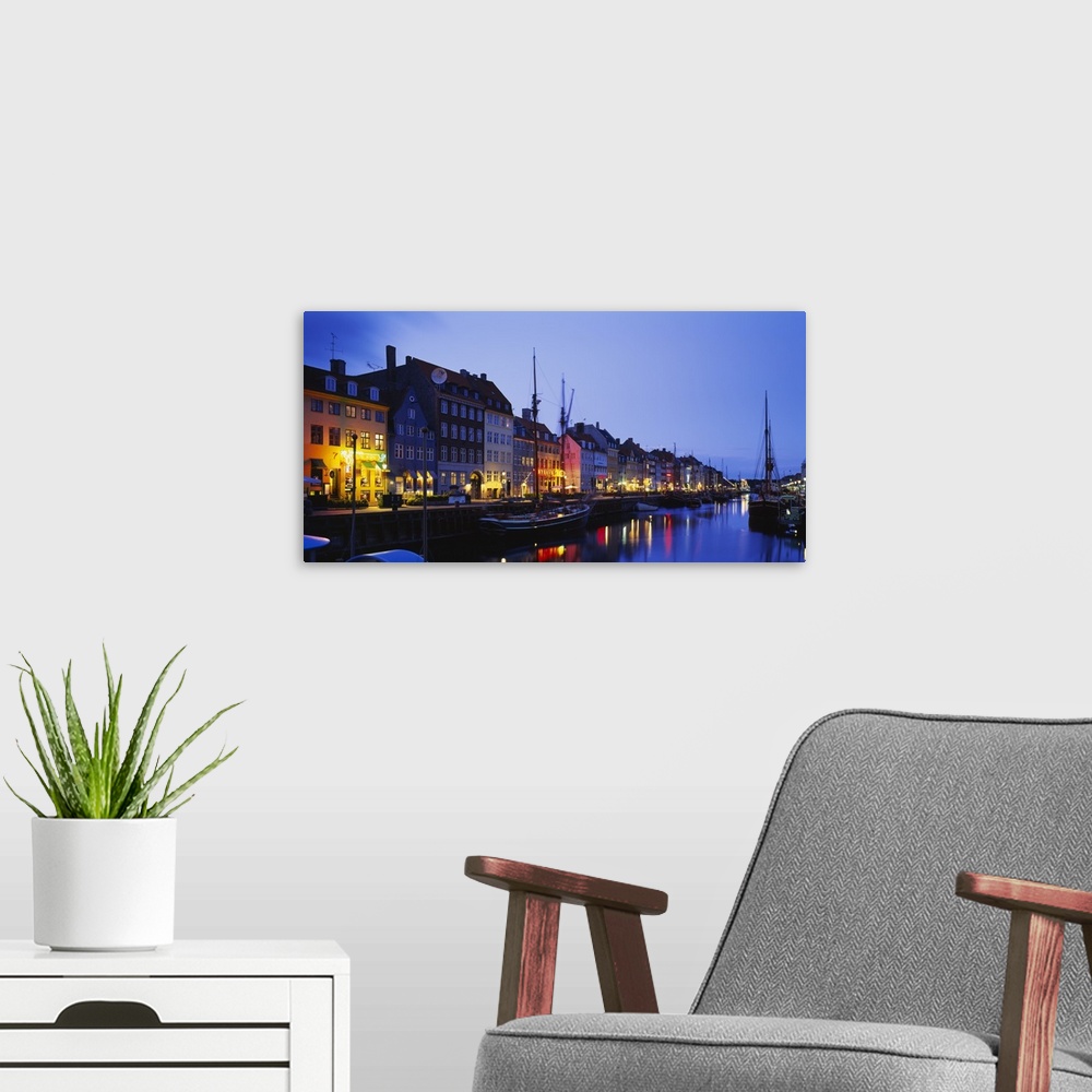 A modern room featuring Big canvas photo of buildings along a street following a waterfront with boats lit up at night.