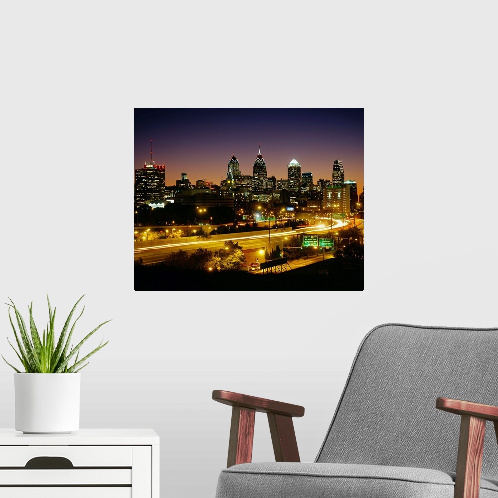 A modern room featuring A time lapsed, landscape photograph showing the light trails of high way traffic entering and lea...