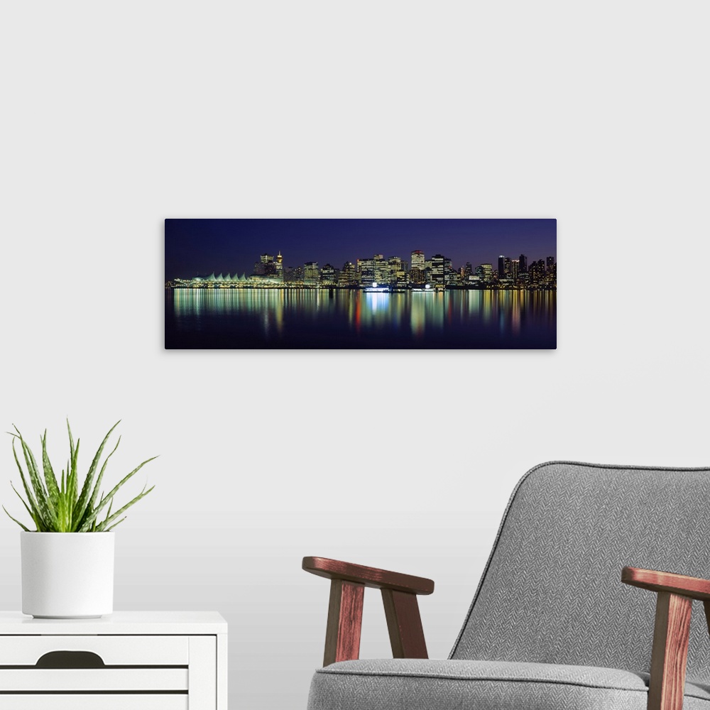A modern room featuring The Vancouver skyline is illuminated under a night sky and the lights reflecting in the water.