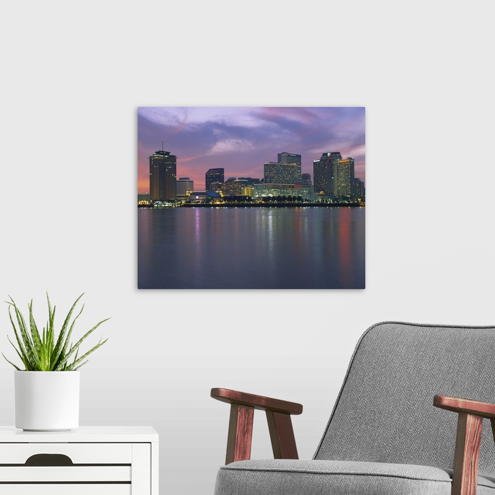 A modern room featuring Panoramic photograph of skyline at waterfront.  The building lights are reflected in the water be...