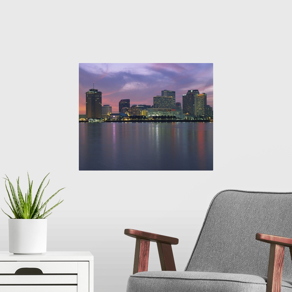 A modern room featuring Panoramic photograph of skyline at waterfront.  The building lights are reflected in the water be...