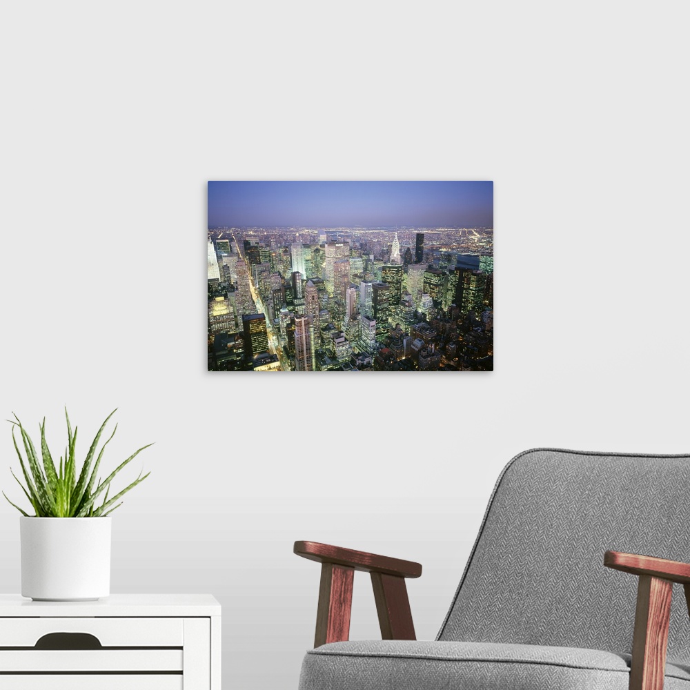 A modern room featuring A photograph taken from the top of a building of the endless city scape illuminated at night.