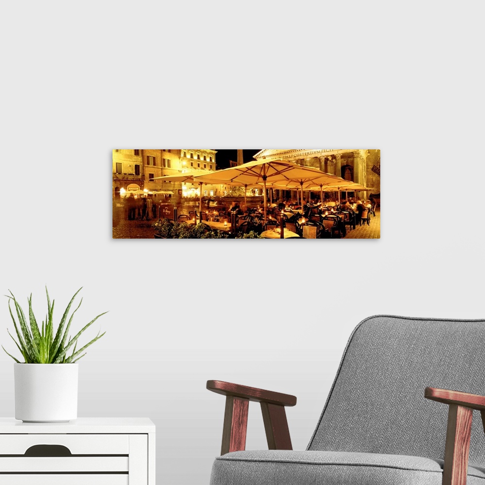 A modern room featuring This panoramic photograph captures a rustic cafo in a plaza in the evening light.